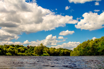 View from the water level on a wide river and a wooded shore, the cone of the roof of a wooden...