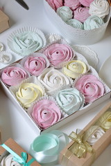 Marshmallows of different colors and shapes. Some in the shape of a flower. Stacked in gift boxes. Nearby are colored ribbons for dressing boxes.