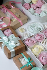 Marshmallows of different colors and shapes. Some in the shape of a flower. Stacked in gift boxes. Nearby are colored ribbons for dressing boxes.