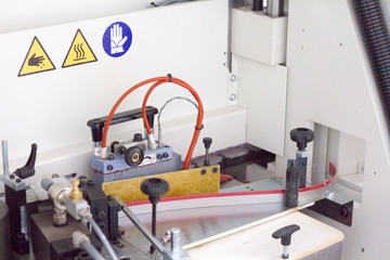 Close-up mechanism of single sided automatic edge banders in a private furniture workshop, selective focus