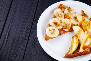 Close up view on breakfast sweet toast with banana and apple poured with caramel on dark background with copy space. Sandwich meal. Food for breakfast.