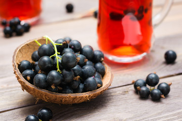 Bowl with black currant berries and fresh compote of ripe black currant in a glass on a wooden table. Close-up