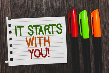 Handwriting text It Starts With You. Concept meaning Motivation for starting doing something Have discipline Colorful words with white page red green orange pen on blackish wooden desk
