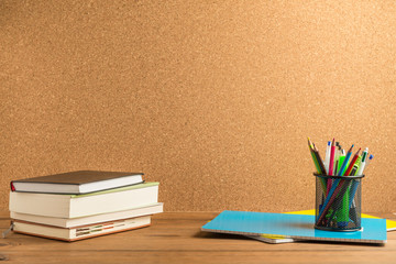 Books, notebooks and school supplies on wooden boards with a cork board in the background.