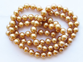 Beautiful mother-of-pearl light beige pastel large beads on a thread on a white fabric isolated object.