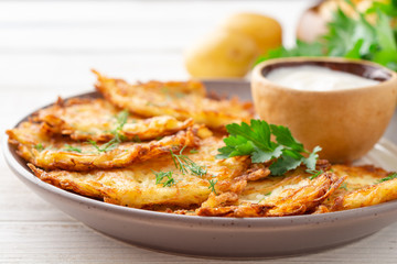 Potato pancakes or latkes or draniki with sour cream in plate on white wooden table. Selective focus.
