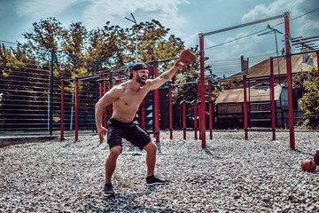 Obraz premium Athletic man working out with a kettlebell at street gym yard. Strength and motivation. Outdoor workout. Exercise for shoulders.