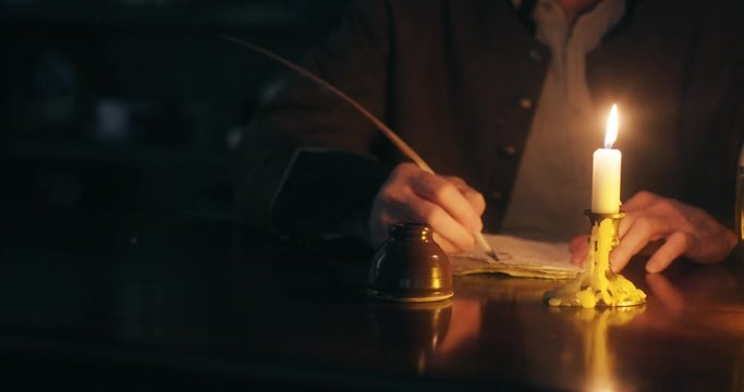wide shot 1700s man writing with quill pen by candle light