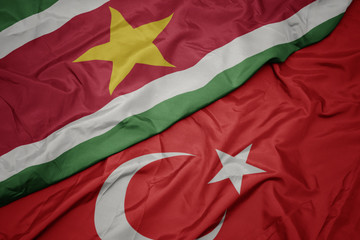 waving colorful flag of turkey and national flag of suriname.