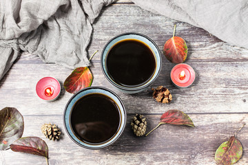 Obraz na płótnie Canvas Romantic hygge autumn composition with two cups of hot aromatic coffee, candles, dry leaves, pine cones on rustic wooden table. Lagom concept.