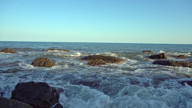 On a rocky shore of the sea. Waves roll with noise onto a rocky shore. Sunrise by the sea. Beautiful seascape. Rocky shore of a stormy ocean. Waves beat against the shore.