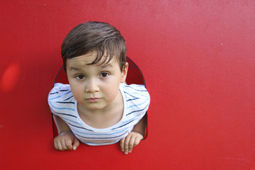 niño mirando por un hueco en una pared roja