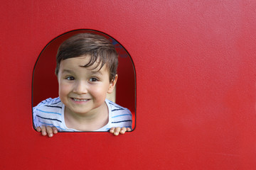 niño mirando por un hueco en una pared roja