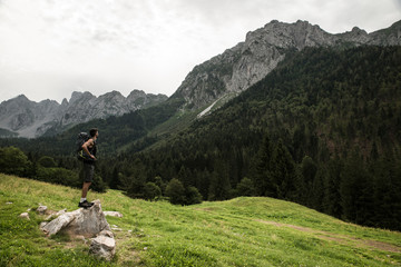 Caucasian man with a trekking backpack standing on a rock and admiring the beautiful mountain landscape