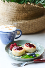 Cheesecakes with raspberry jam, berries and mint leaves served with a cup of latte