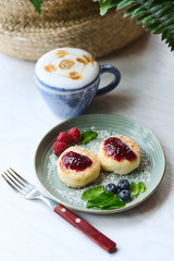 Cheesecakes with raspberry jam, berries and mint leaves served with a cup of latte