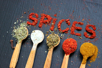 The word spice is written on a black background. Various spices ground turmeric pepper ginger cinnamon herb seasoning salt paprika cumin wooden vintage spoon on black table. The view from the top. Spi