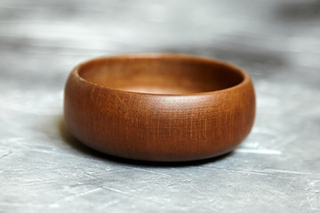 One empty wooden bowl on grey background. Single round salad bowl on stone table with black paint stains, side view