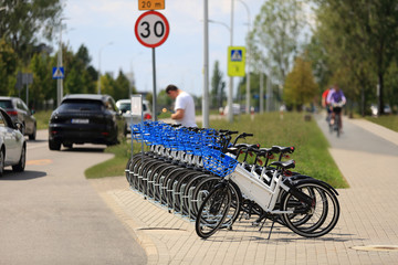 Rowery, mężczyzna przy stacji wypożyczania rowerów przy drodze, samochody i rowerzyści.