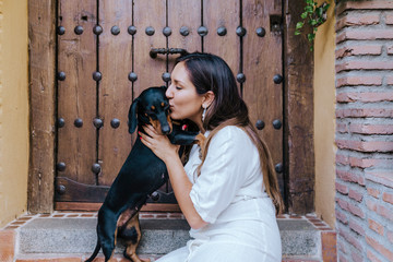 cute small sausage dog sitting outdoors with her owner at home. Woman kissing her dog. Love for...