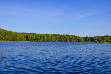 View of a blue lake or river on a sunny day on a background of blue sky and green forest.