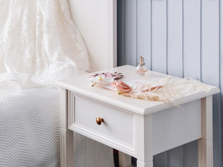 Gray bedside table with bridal accessories. Decorative monstera leaves and pampas grass, pale pink rose flowers and a bottle of perfume.