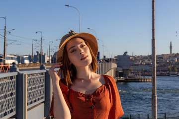 Beautiful girl with orange colored dress posing with the Galata Bridge and Mosques from Istanbul