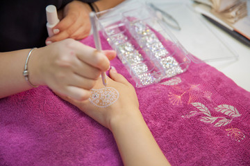 the master draws in the form of a buta feather on his hand with white gel . street artist draws henna patterns on his hand on a city holiday . Pink varnish on the nail . Draws henna into his hands .