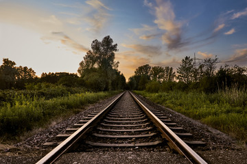 Railroad track through distant rural landscape at sunset