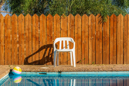 suburban villa back yard of swimming pool privacy space for spending free time for rest with ball on water surface and white plastic chair on wooden fence background 