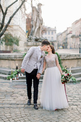 Romantic wedding couple in love, walking and kissing, holding hands. Wedding decor on the stone stairs, monument, ancient buildings on the background