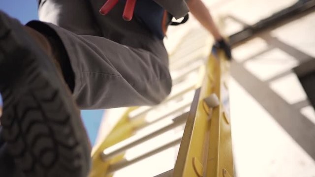 Pull-out downwards shot of a fiber optics technician wearing protective gear going down a ladder