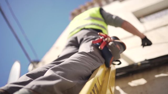 Low Upwards shot or a technician in protective gear on a ladder installing optical fiber cables on a building