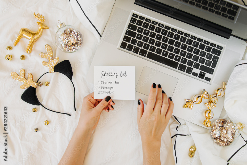 Wall mural Young woman shopping online for christmas holiday.  Laptop with Christmas decorations on white bed with a blanket. Holiday concept. Flat lay, top view