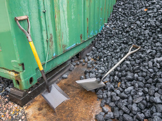 Two shovels next to a shipping container and a pile of coal
