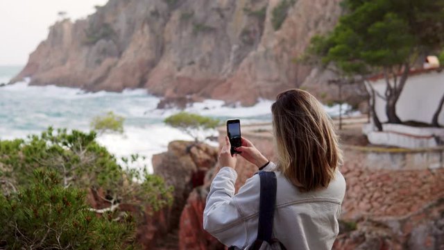 Back view on brunette millennial girl taking photos of sea view