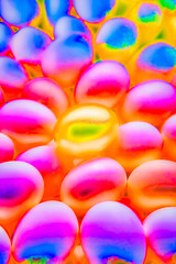 Golden egg sitting in the middle of a field of rainbow colored eggs.