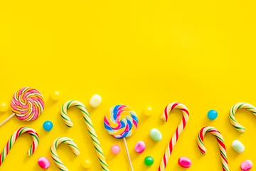 Keuken spatwand met foto Assorted sweets, lollipop and candy cane on yellow background top view mock up © 9dreamstudio