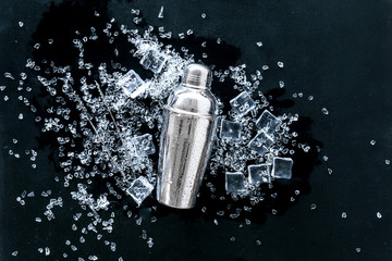 Pile of ice cubes and shaker on black bar desk background top view