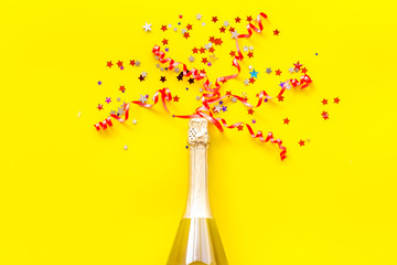 Champagne bottle with colorful party streamers for celebration on yellow background top view