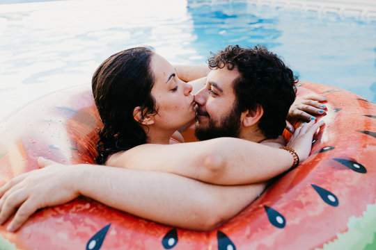 Young couple on inflatable watermelon in swimming pool at hotel. Woman kisses her boyfriend nose. Summer holiday, lifestyle concept. Love moment.