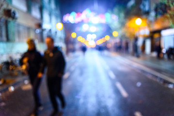 Urban night scene with people walking out of focus with colored background.