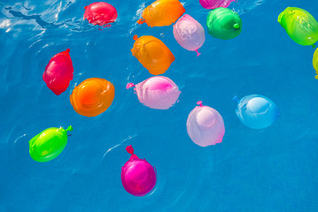 Group of many colorful plastic water balloons floating in the water of a pool to entertain their...