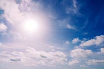 Naklejka na ściany i meble Glowing sun in a blue summer sky with nice white clouds.