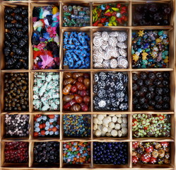 Many different, colorful glass beads, sorted in a wooden box.