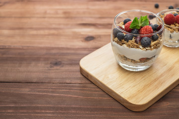 Healthy yogurt grain and berries dessert glass on top of a wooden tray on wood surface background.
