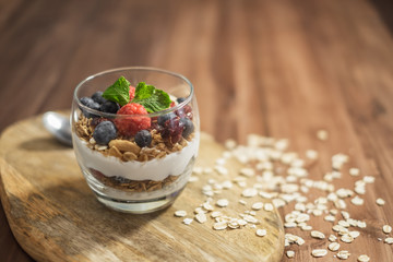 Healthy yogurt grain and berries dessert glass on top of a wooden tray on wood surface background.