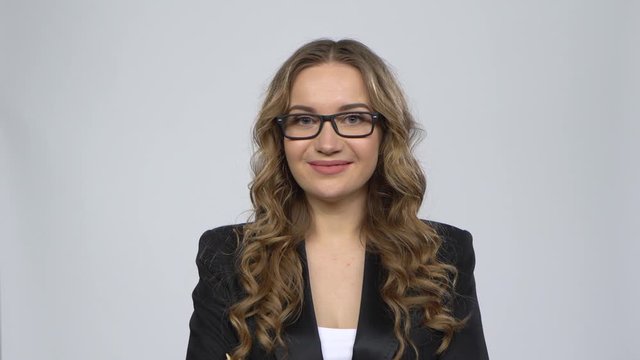 Bussines woman looks at the camera with a smile, takes off her glasses and a dream about something against grey background