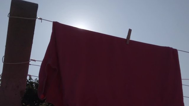 Sun-flare on pink laundry on a clothesline in backlight, vertical up dolly shot in slow motion