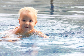 Fototapeta na wymiar Cute baby swims in a swimming pool in summer